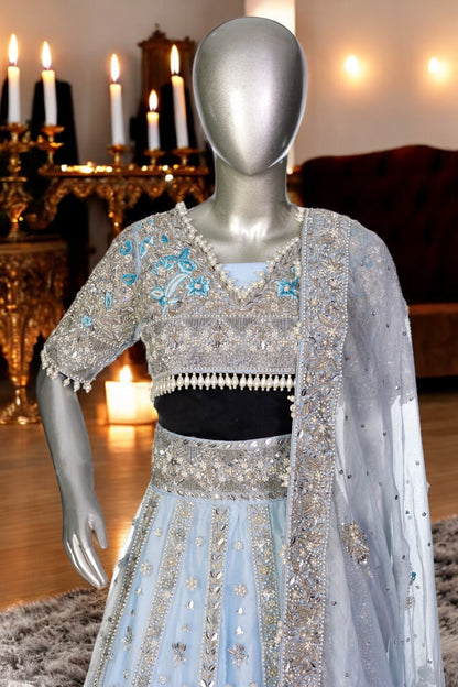 Elsa – Ice blue Pakistani bridal lehenga by MariamRaj featuring a hand-embroidered raw silk blouse with tassels, net lehenga with intricate motifs, and a fully embellished net organza dupatta. Custom stitched for Pakistani brides in USA and UK.