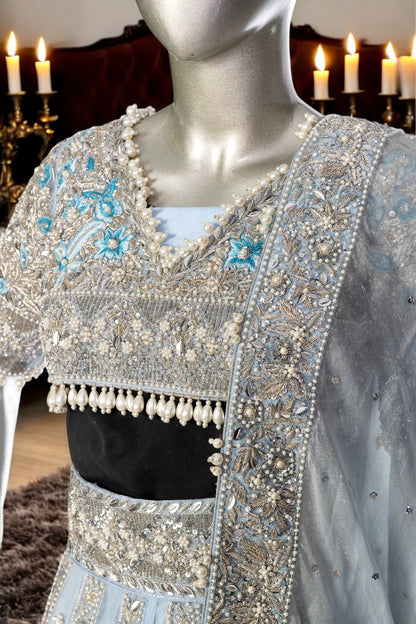 Elsa – Ice blue Pakistani bridal lehenga by MariamRaj featuring a hand-embroidered raw silk blouse with tassels, net lehenga with intricate motifs, and a fully embellished net organza dupatta. Custom stitched for Pakistani brides in USA and UK.