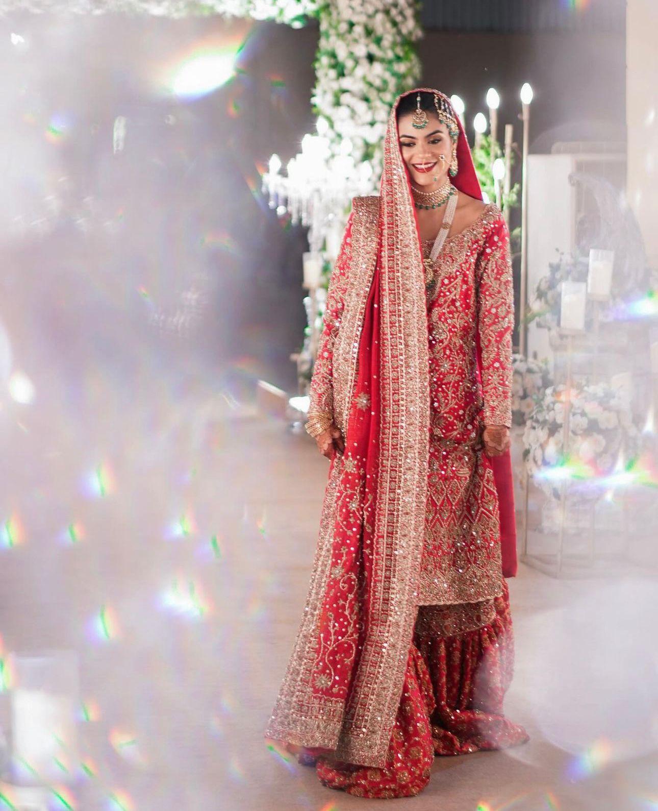 Red bridal farshi gharara by MariamRaj featuring embroidered raw silk kameez, brocade silk gharara, and embellished khaadi silk dupatta – ideal for baraat and Pakistani weddings.