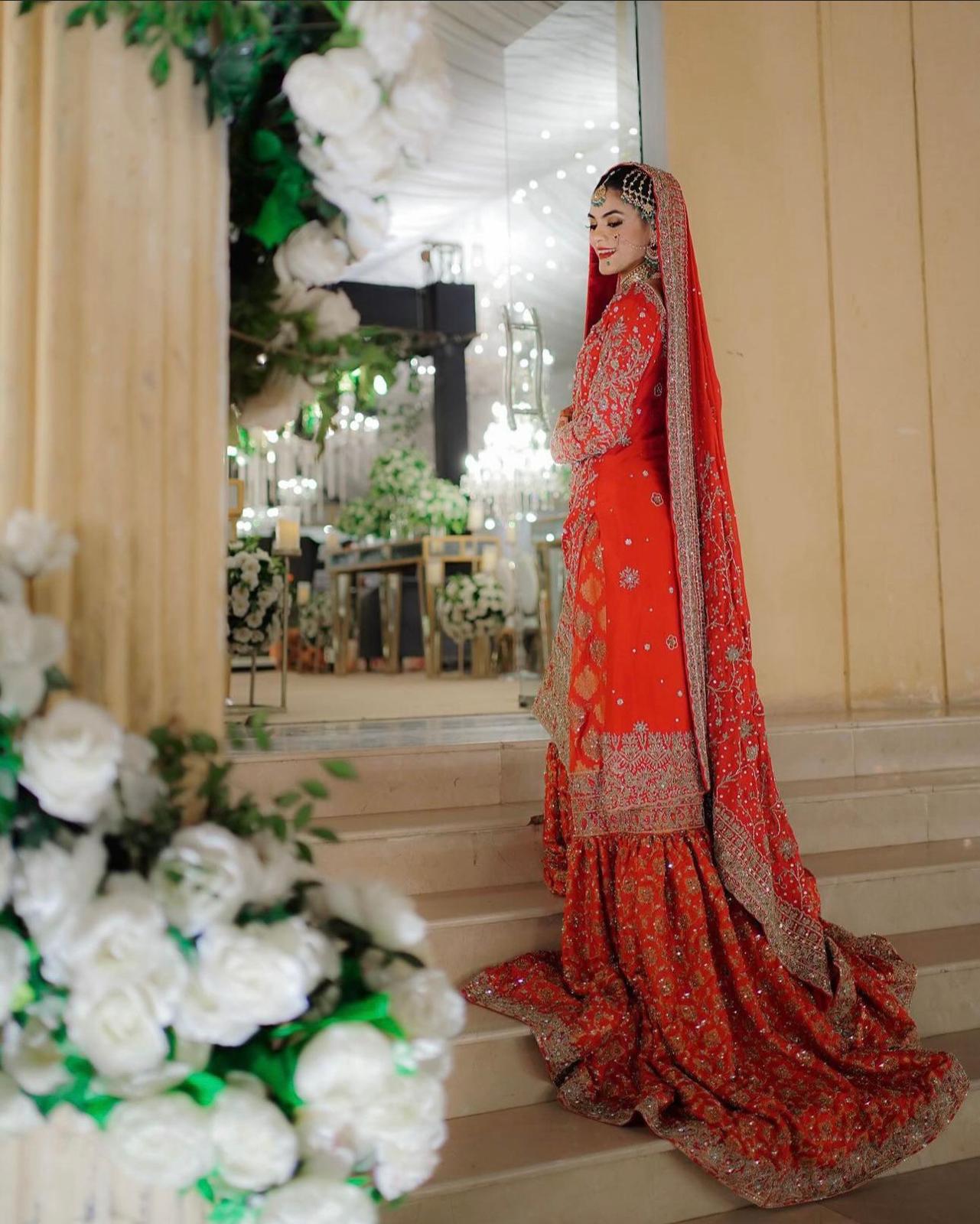 Red bridal farshi gharara by MariamRaj featuring embroidered raw silk kameez, brocade silk gharara, and embellished khaadi silk dupatta – ideal for baraat and Pakistani weddings.